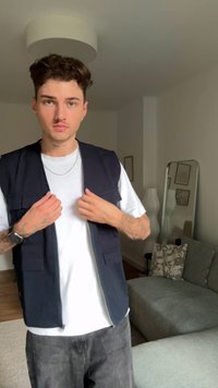 Marineblaues ärmelloses Weste mit Fronttaschen, getragen über einem weißen T-Shirt. Verfügt über eine lässige Passform und strukturierten Stoff. Einfache Hintergrundelemente sichtbar.