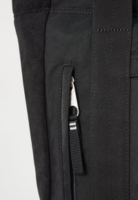 Zaino in tessuto nero con superficie testurizzata, una tasca laterale con zip e una tracolla con un elegante accessorio in metallo.