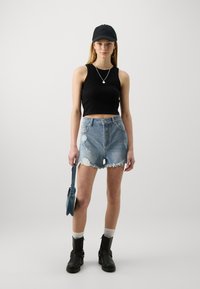 Čierny crop top, roztrhnuté denimové šortky, členkové topánky a malá denimová taška. Pozoruhodné detaily zahŕňajú rozstrapkaný lem a strieborné kruhové náušnice.
