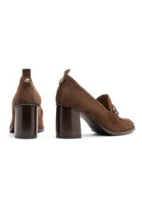 Brown suede heeled shoes with a rounded toe, mid-height block heels, and a metallic accent detail. Features a stitched design and back pull tab.
