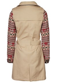 Beige trenchcoat met gestreepte mouwen in rood, zwart en crème. Voorzien van een riem, knoopmanchetten en een rugventilatie. Gladde textuur.