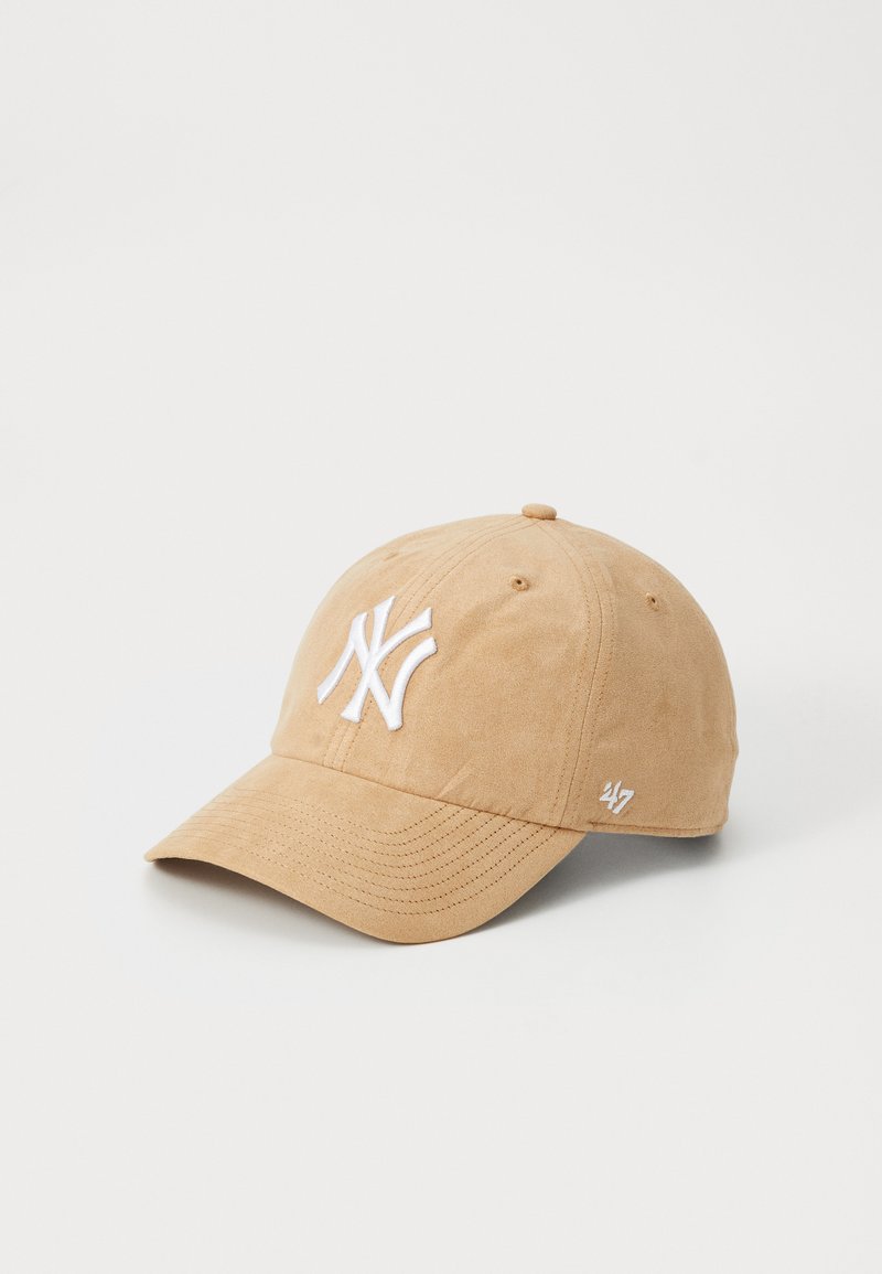 Tan suede baseball cap featuring a white embroidered logo on the front, curved brim, and a small white graphic on the side.