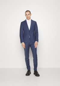 Navy blue slim-fit suit with single button closure, notch lapels, side pockets, paired with a white shirt and black shoes.