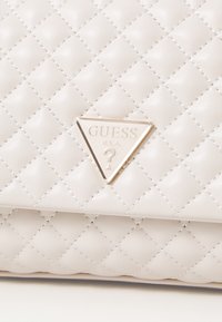 Quilted white leather handbag with a triangular gold logo. Features diamond pattern stitching and subtle shine. Compact and structured design.