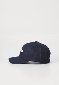 Marineblaue Denim-Baseballmütze mit gebogenem Schirm und weißem, gesticktem Logo auf der Vorderseite. Sechspaneldesign mit Belüftungsösen.