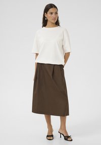 Valge lühikeste varrukatega tops koos pruuni midi seelikuga, millel on taskud ja sile tekstuur. Mustad kontsakingad, millel on kaariku aksendid.