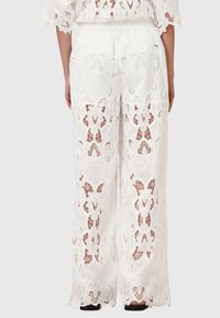 Valkoiset pitsihousut, joissa on kukkakuosi, leveät lahkeet ja joustava vyötärö. Kankaat ovat läpikuultavia ja niissä on monimutkaisia leikattuja yksityiskohtia.