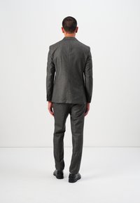 Costum gri, croit cu un material texturat. Sacoul are o deschidere simplă, iar pantalonii au o croială dreaptă. Purtați cu pantofi negri de dress.