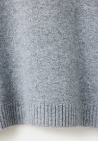 Gros plan de l'ourlet d'un pull tricoté doux gris clair avec une texture côtelée le long du bord inférieur.
