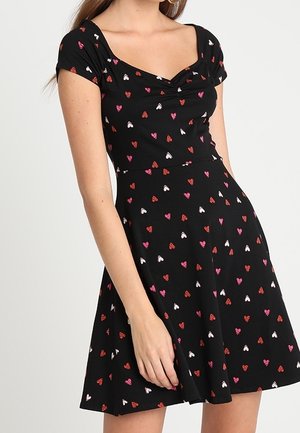 Robe noire à manches courtes avec un décolleté en cœur, dotée d'une jupe évasée et d'un motif de petits cœurs rouges, roses et blancs.