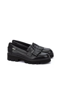 Mocasines de cuero negro con detalle de flecos, que presentan una suela de goma gruesa, una textura suave y un acento de logo en el lado.