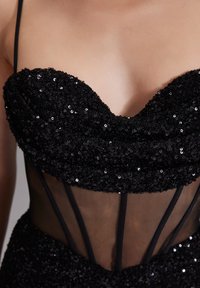Robe en sequins noirs avec un corsage ajusté, un décolleté en cœur et des détails en maille transparente avec de fines bretelles noires.