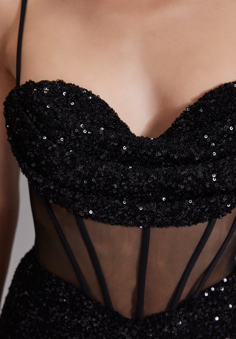Robe en sequins noirs avec un corsage ajusté, un décolleté en cœur et des détails en maille transparente avec de fines bretelles noires.