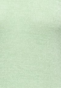 Gros plan sur un tissu tricoté doux de couleur vert clair avec un motif de points lisse et uniforme et de légères variations de texture.