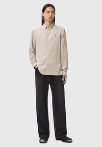 Camicia button-up beige chiaro in tessuto morbido con maniche lunghe, abbinata a jeans in denim scuro a vestibilità ampia e scarpe nere con accenti argentati.