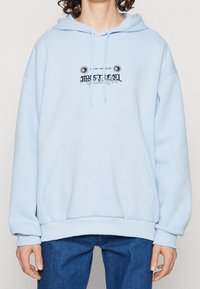 Jasnoniebieska bluza z kapturem wykonana z miękkiego materiału, z przednią kieszenią i czarnym graficznym wzorem tekstowym z motywami słonecznymi.