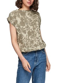 Beżowa bluzka w kwiaty z lekkiego materiału. Krótkie rękawy z podwójnym złożeniem, okrągły dekolt, zestawiona z niebieskimi dżinsami.