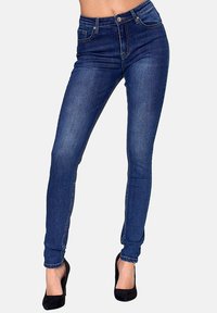 Skinny jeans in dark blue denim, high-waisted design, five pockets, with visible stitching and a smooth texture. Paired with black heels.