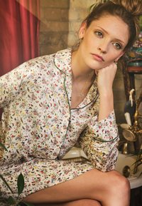 Yhdistelmä kukkaprinttiyöpuvusta, jossa on vaalea tausta, vihreät yksityiskohdat ja rento istuvuus. Kuosisuunnittelu sisältää perhosia ja kukkia.