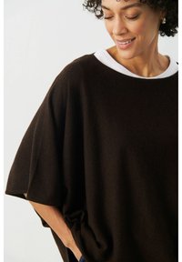 Bruine oversized trui met een witte ronde hals, met een losse pasvorm en een zachte textuur. Het ontwerp heeft zijzakken voor een extra detail.