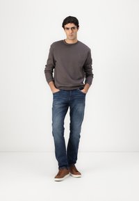 Szürke pulóver, kék farmernadrág és barna sportcipő. Az öltözet laza, kényelmes szabású, kerek nyakú, és a szokásos farmer textúrával rendelkezik.