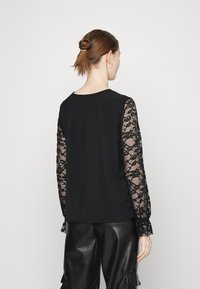 Blusa preta com mangas longas em renda com padrões florais. Tecido texturizado e corte descontraído com decote arredondado, combinada com calças de couro pretas.