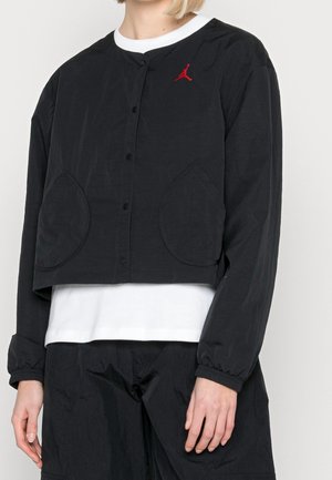 Chaqueta negra corta con cierre de botón, mangas largas, dos grandes bolsillos de parche y un logo rojo en el lado izquierdo del pecho. Material de mezcla de algodón.