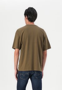 Olivově zelené tričko s krátkým rukávem a kulatým výstřihem, vyrobené z hebké bavlny. V páru s tmavě modrými džíny s jemným designem kapsy.