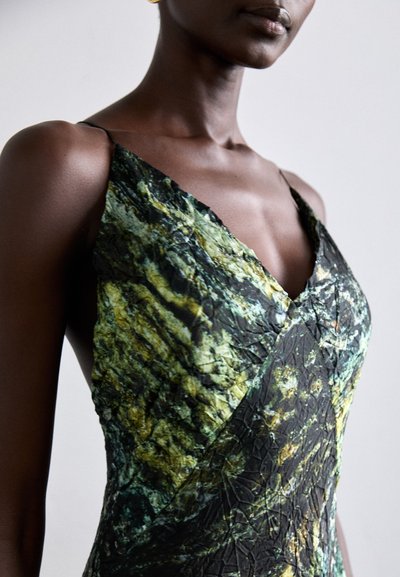 Vestido de satén con escote en V profundo, patrón abstracto en verde y negro, con tirantes finos y superficie texturizada.
