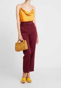 Cowl-neck satin top in golden yellow, high-waisted maroon trousers, woven basket handbag in light yellow, and yellow block-heeled sandals.
