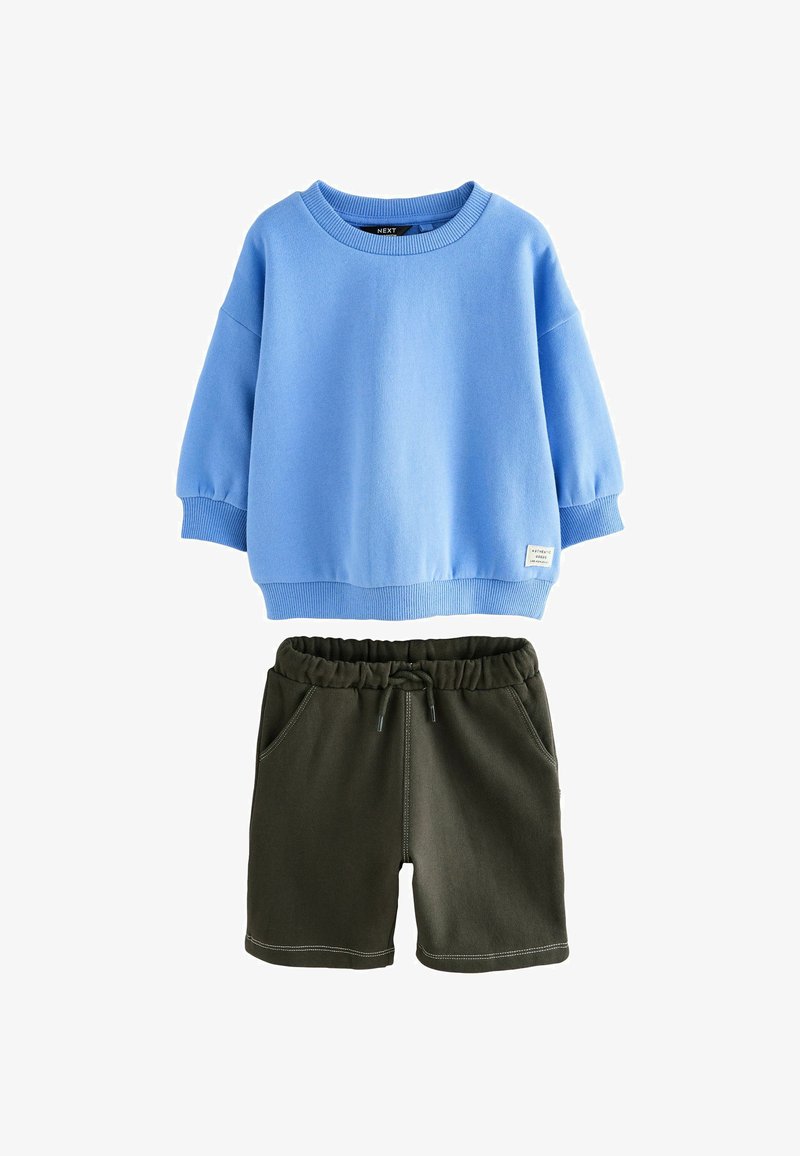 Mėlyna ilgomis rankovėmis sportinė maikė su gumuotomis rankovėmis ir apdaila, derinama su tamsiai žaliais elastingais šortais, turinčiais priekines kišenes ir raištelį.