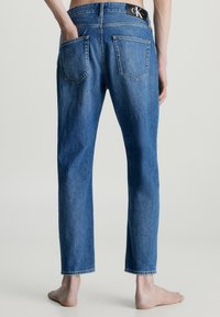 Jeans de denim azul claro con corte recto, que cuentan con dos bolsillos traseros, una etiqueta de marca visible en la cinturilla y dobladillos sin terminar.