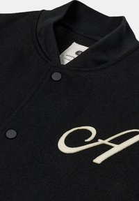 Giacca varsity nera con finitura in lana testurizzata, dotata di colletto a costine, bottoni snap neri e una grande lettera "A" ricamata in bianco.