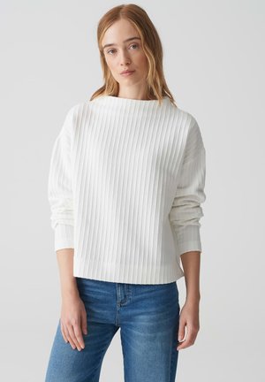 Witte geribde trui met een bootnek en lange mouwen. Kenmerkt zich door horizontale textuurstrips en een relaxte pasvorm, gecombineerd met blauwe jeans.
