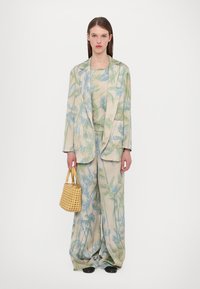 Floral-patterned blazer and wide-leg pants in cream, blue, and green. Model holds a small, woven yellow handbag. Black footwear.