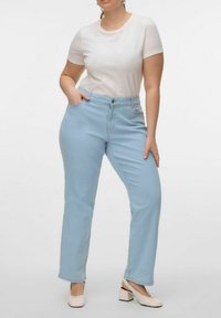 Jeans de pierna recta azul claro con cintura alta, bolsillos frontales y cierre de botón, combinados con una camiseta blanca ajustada y zapatos de tacón cuadrado beige.