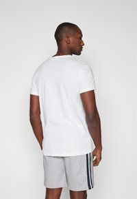 White short-sleeve t-shirt, crew neck, made of cotton. Worn with gray shorts featuring horizontal stripes in blue and green.