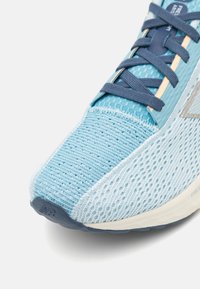Zapatilla deportiva azul clara con parte superior de malla texturizada, cordones azul oscuro y suela de goma que presenta un logotipo en relieve en el talón.