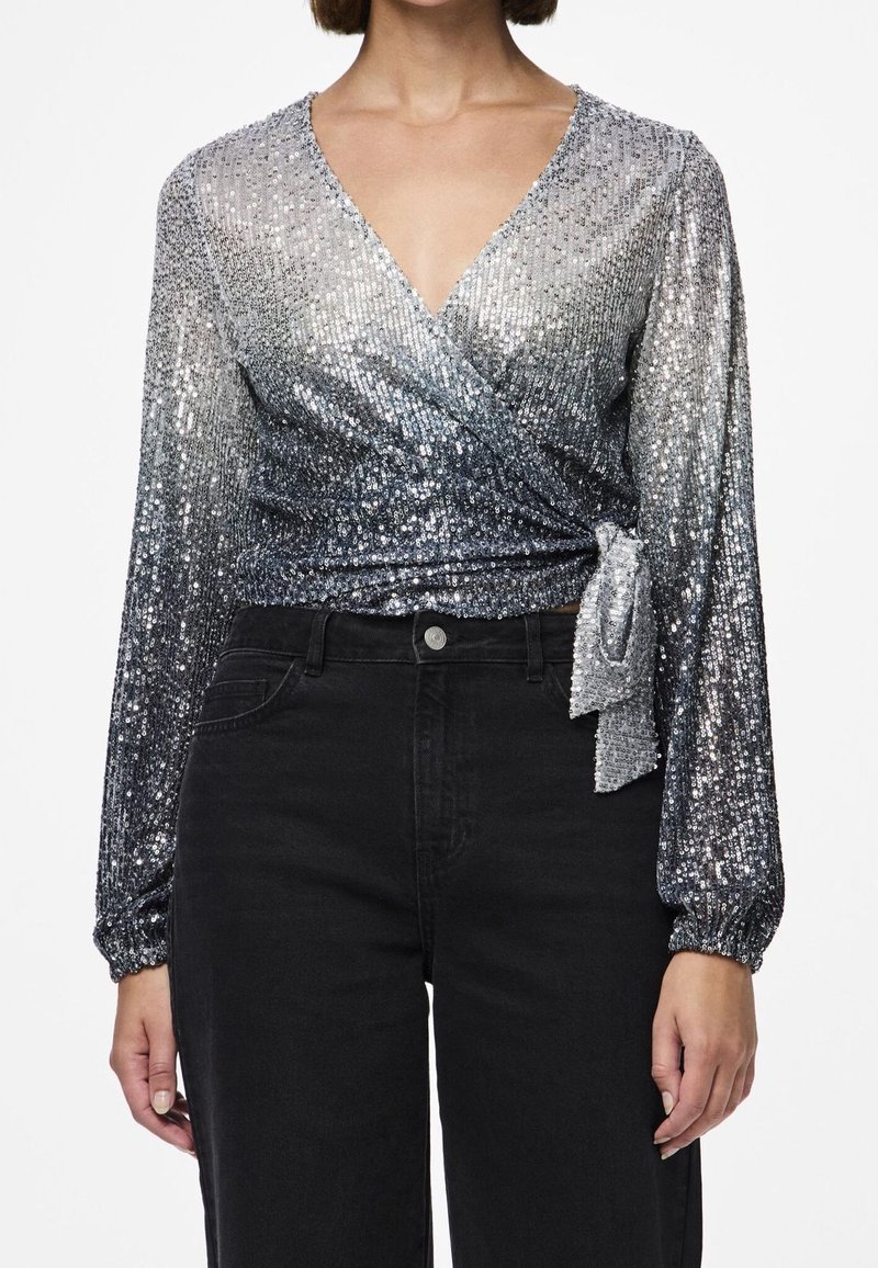 Haut portefeuille à manches longues avec sequins argentés et nœud sur le côté, associé à un jean noir taille haute, présenté des épaules aux hanches.