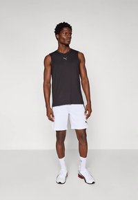 Μαύρο αμάνικο μπλουζάκι με λογότυπο, συνδυασμένο με λευκά σορτς. Απλός σχεδιασμός, ελαφρύ ύφασμα και άνετη εφαρμογή, μαζί με λευκά αθλητικά παπούτσια.