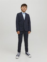 Abito blu navy con giacca a singolo bottone e pantaloni slim-fit abbinato a una camicia azzurra e sneakers blu con accenti bianchi.