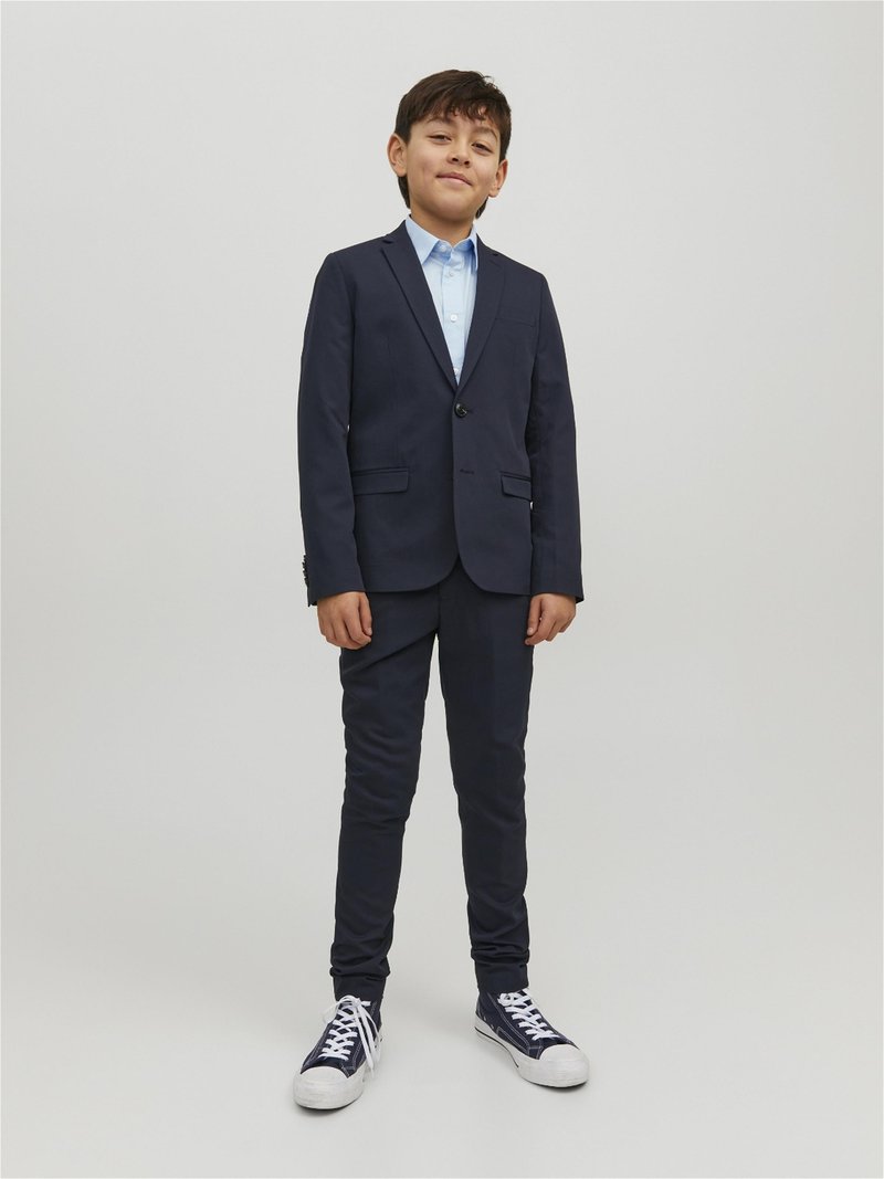 Abito blu navy con giacca a singolo bottone e pantaloni slim-fit abbinato a una camicia azzurra e sneakers blu con accenti bianchi.