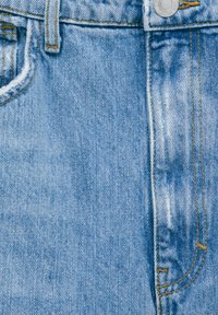 Jean en denim bleu clair avec une texture décolorée, des coutures visibles en jaune contrastant, et une fermeture à bouton en métal à la taille.