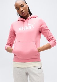 Ροζ φούτερ με κουκούλα από βαμβακερό μείγμα ύφασμα, με μπροστινή τσέπη, ρυθμιζόμενη κουκούλα με κορδόνι και λευκό λογότυπο "PUMA" τυπωμένο εμφανώς στο στήθος.