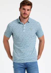 Camisa polo azul claro con un diseño estampado y un cuello en contraste. Tiene tres botones y mangas cortas. Tejido de textura suave.