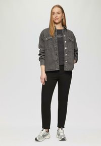 Czarna kurtka dżinsowa z zapięciem na guziki, dwiema kieszeniami na piersi i kontrastowymi szwami, noszona na czarnej koszuli, w połączeniu z czarnymi dżinsami i srebrnymi trampkami.