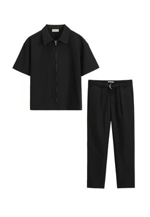 Chemise noire à manches courtes avec fermeture éclair associée à un pantalon noir cintré comportant une boucle de ceinture avec un détail en anneau métallique. Texture de tissu lisse.
