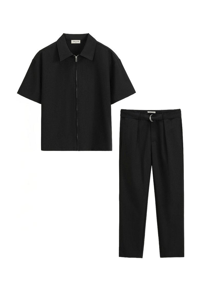 Chemise noire à manches courtes avec fermeture éclair associée à un pantalon noir cintré comportant une boucle de ceinture avec un détail en anneau métallique. Texture de tissu lisse.