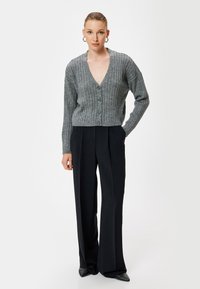 Cárdigan de punto gris con un escote en V profundo, textura acanalada y cierre de botones, combinado con pantalones de pierna ancha negros y zapatos de tacón puntiagudos.