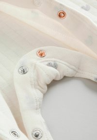 Valge kanga lähivõte koos hõbedaste ja vasksete trukkidega volditud riideäärel.